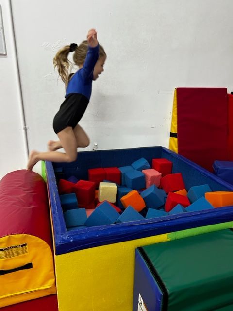 A toddler girl is learning skills in a gymnastics class