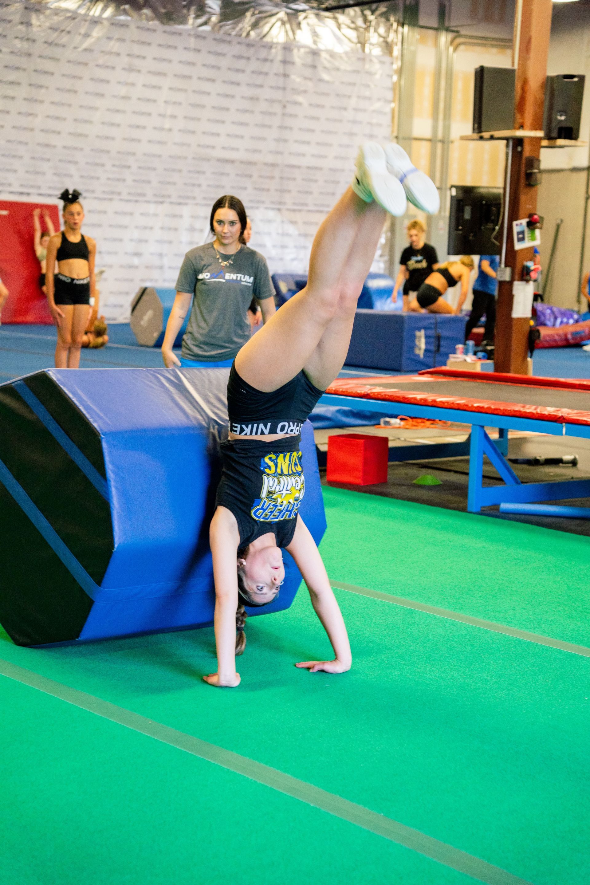 a coach is helping a girl learn beginner tumbling skills
