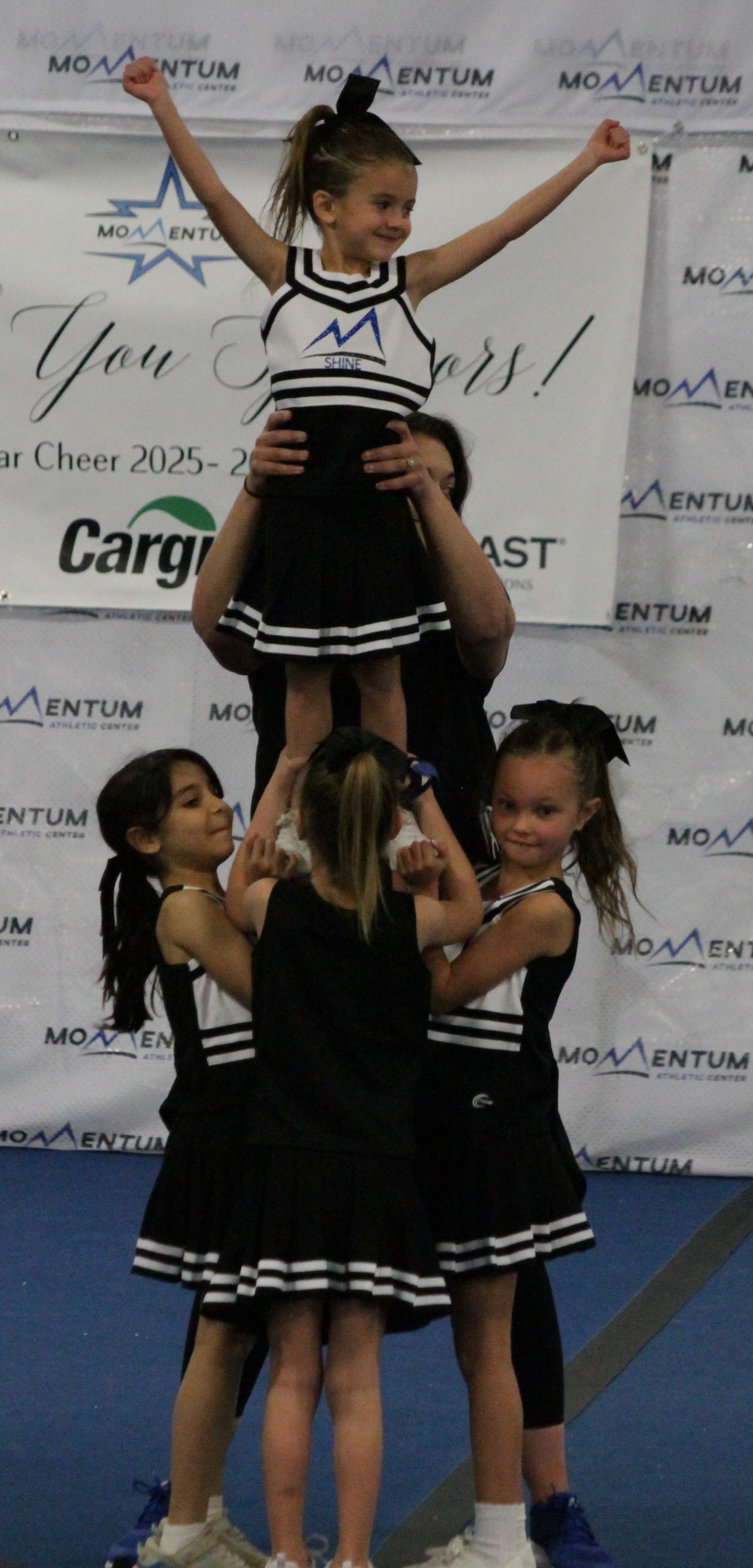 Cheerleaders lifting a teammate overhead during a performance on a blue mat.