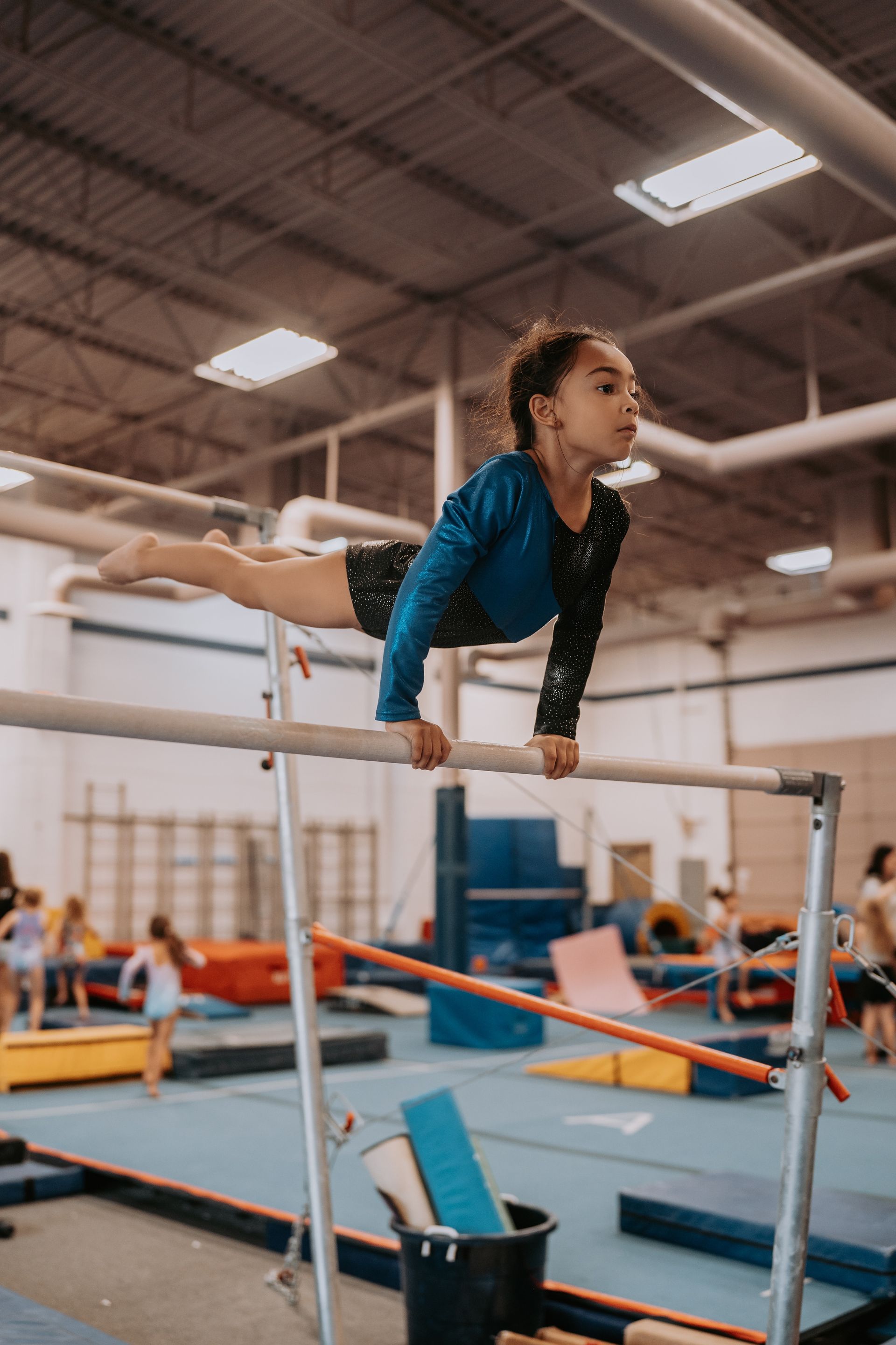 A young girl is doing a split on a parallel bars in a gym.