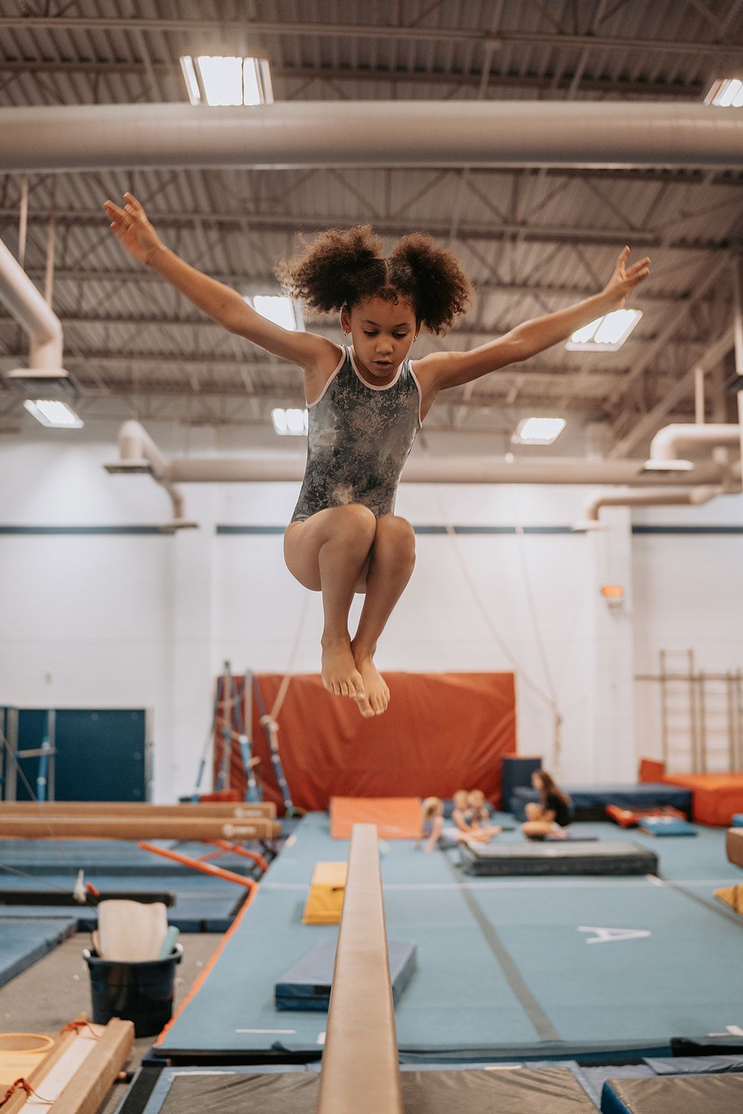 A young girl is doing a split on a parallel bars in a gym.