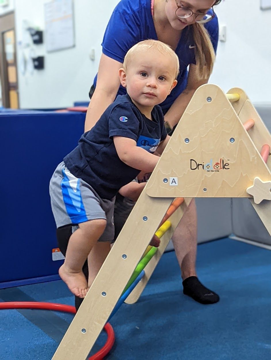 A woman is helping a little boy climb a wooden ladder.