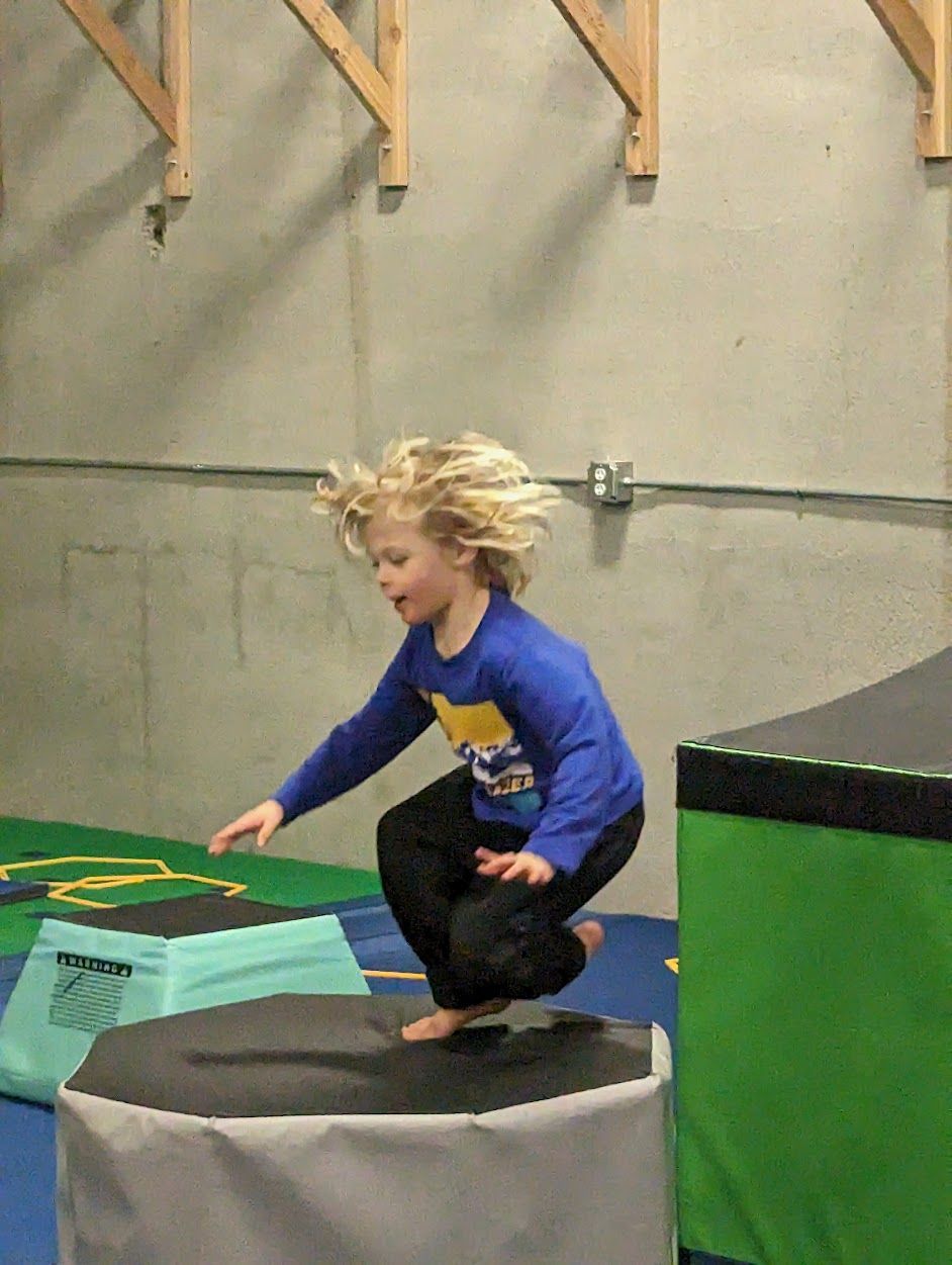 A young boy is jumping over a box in a gym.