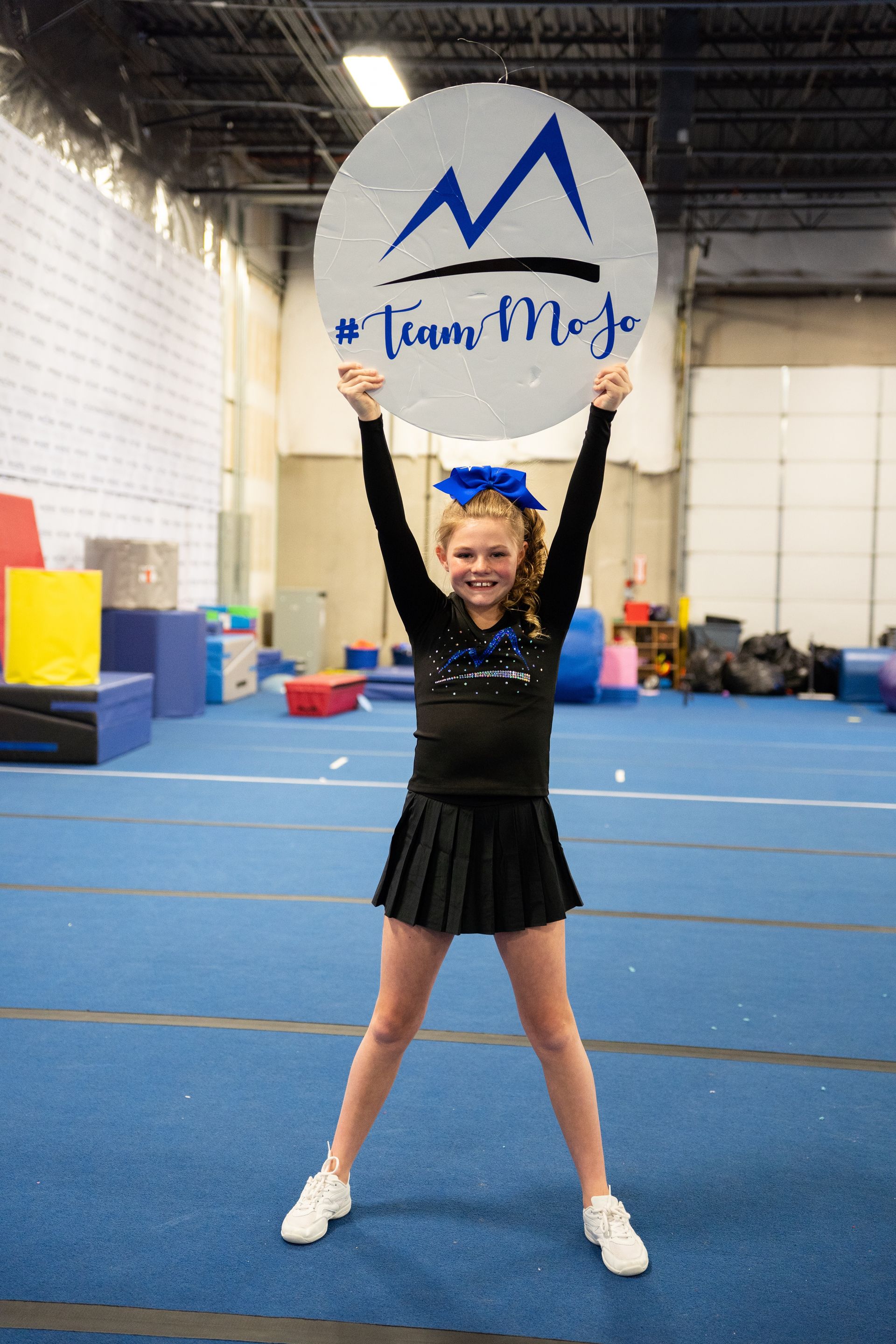 A female vcheerleader is holding up a Momentum sideline cheer sign before a performan