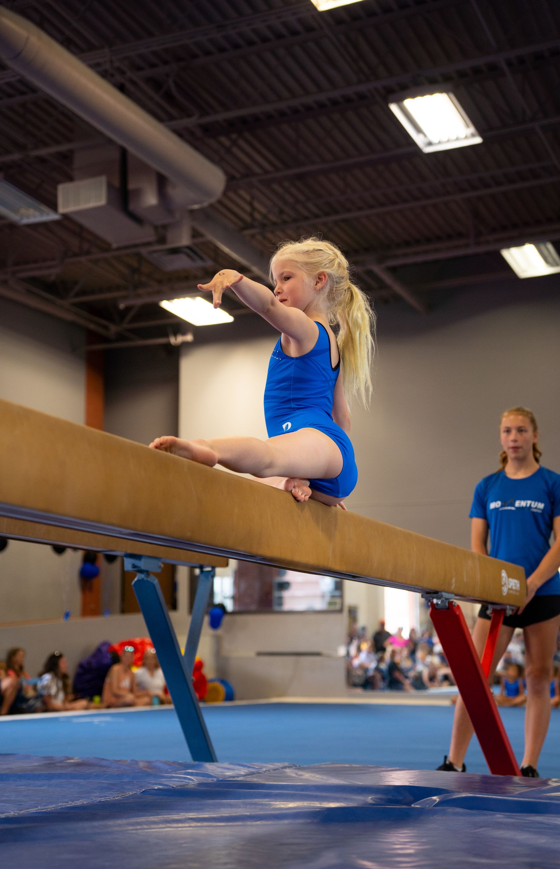 A young girl is sitting on a balance beam in a gym.