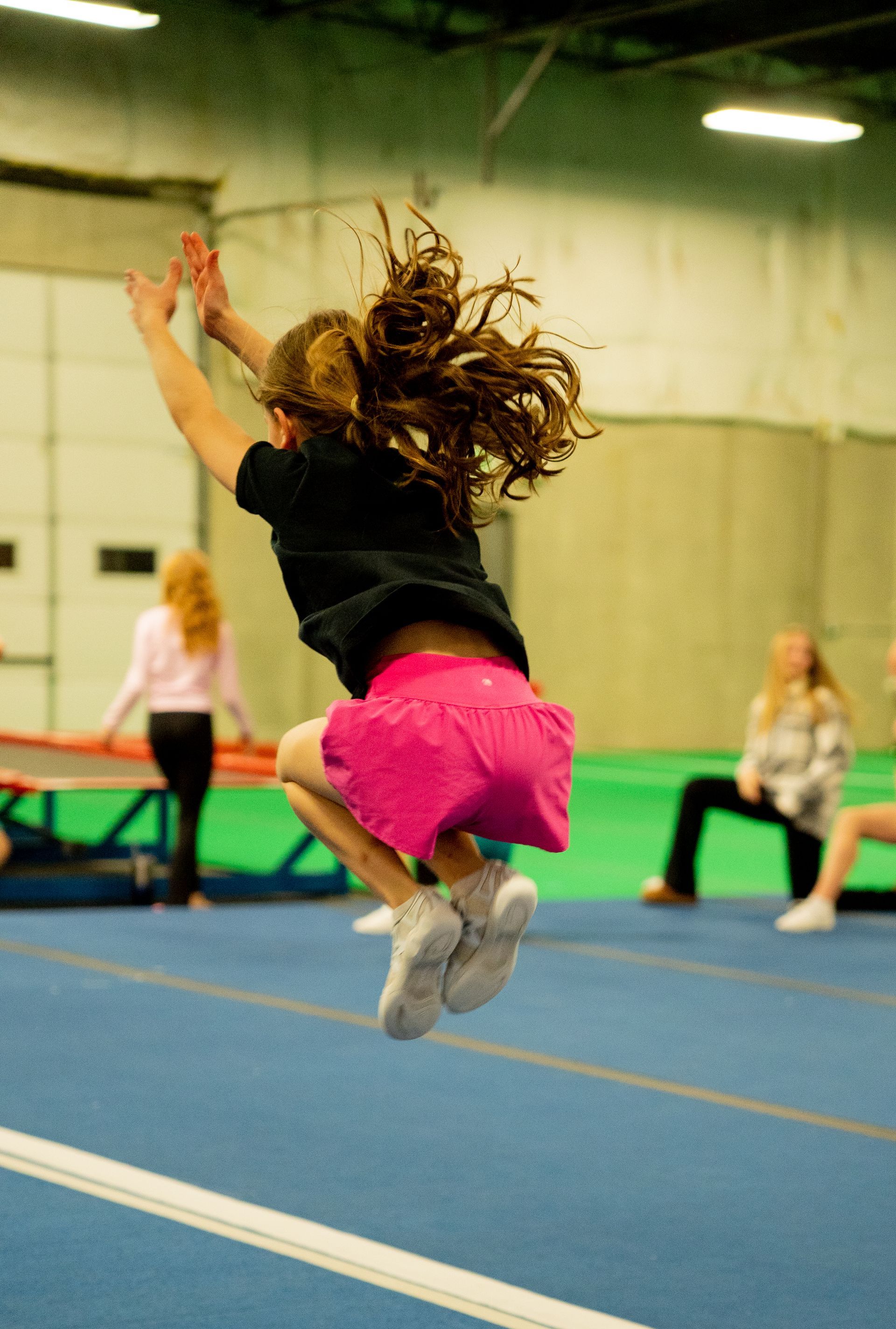 A young girl is jumping over a balance beam in a gym.