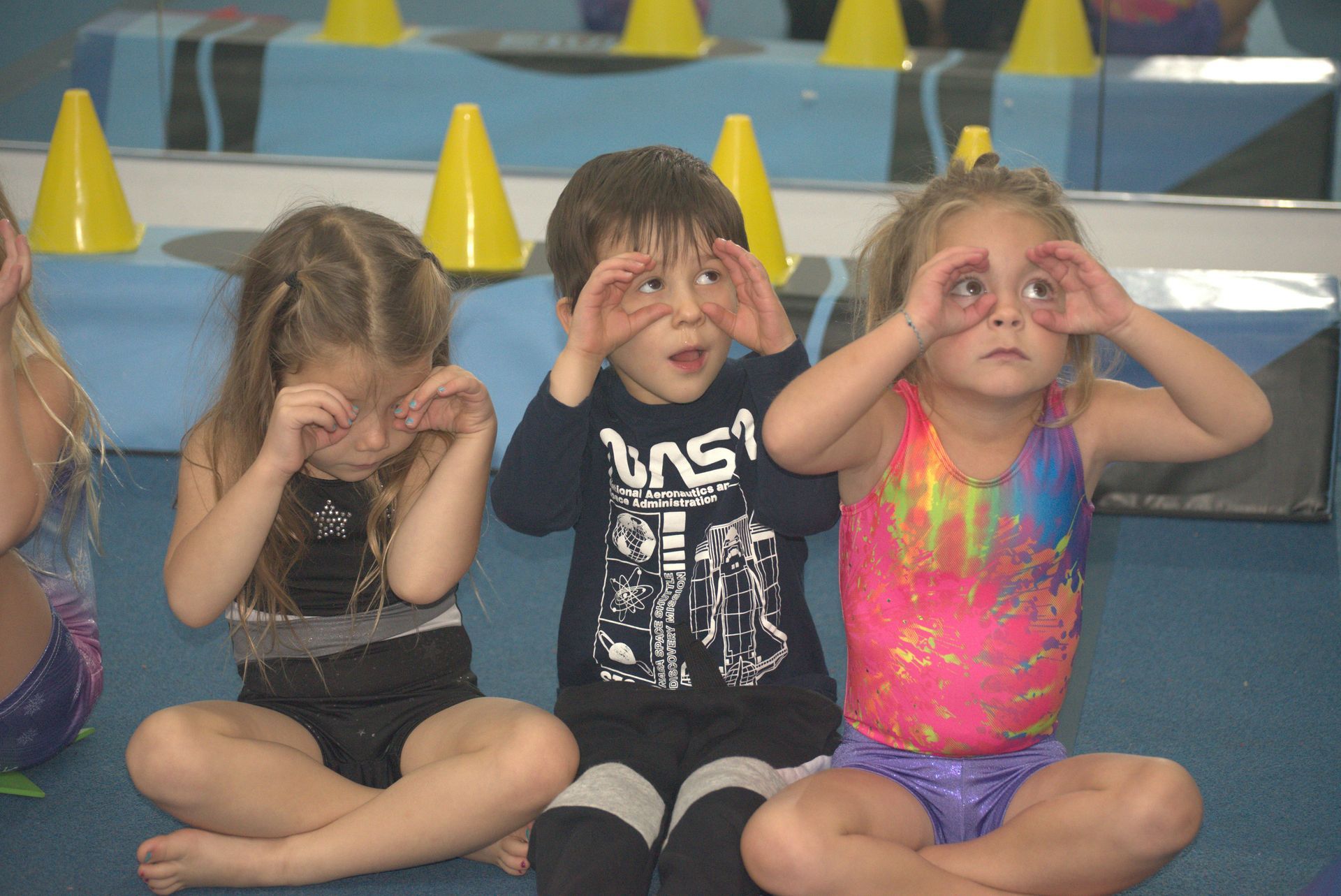 A boy and two girls are sitting on the floor covering their eyes with their hands.