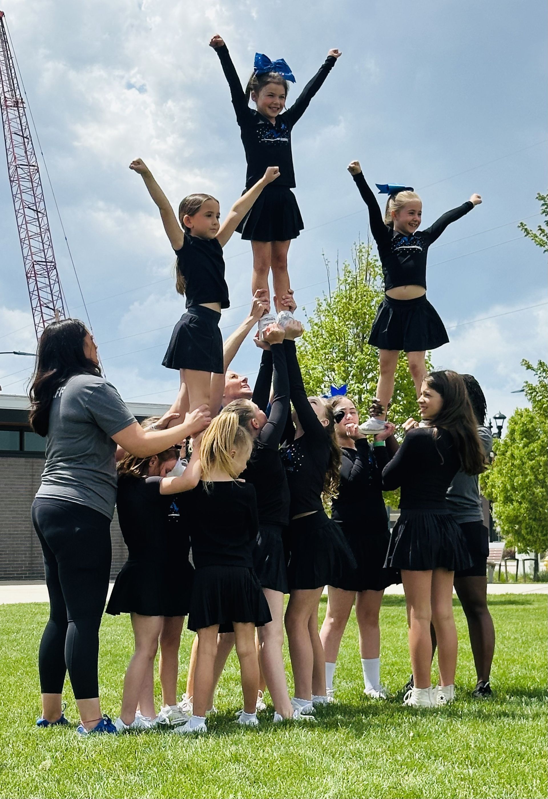 Cheerleaders in black uniforms building a pyramid on a grassy field; blue sky background.