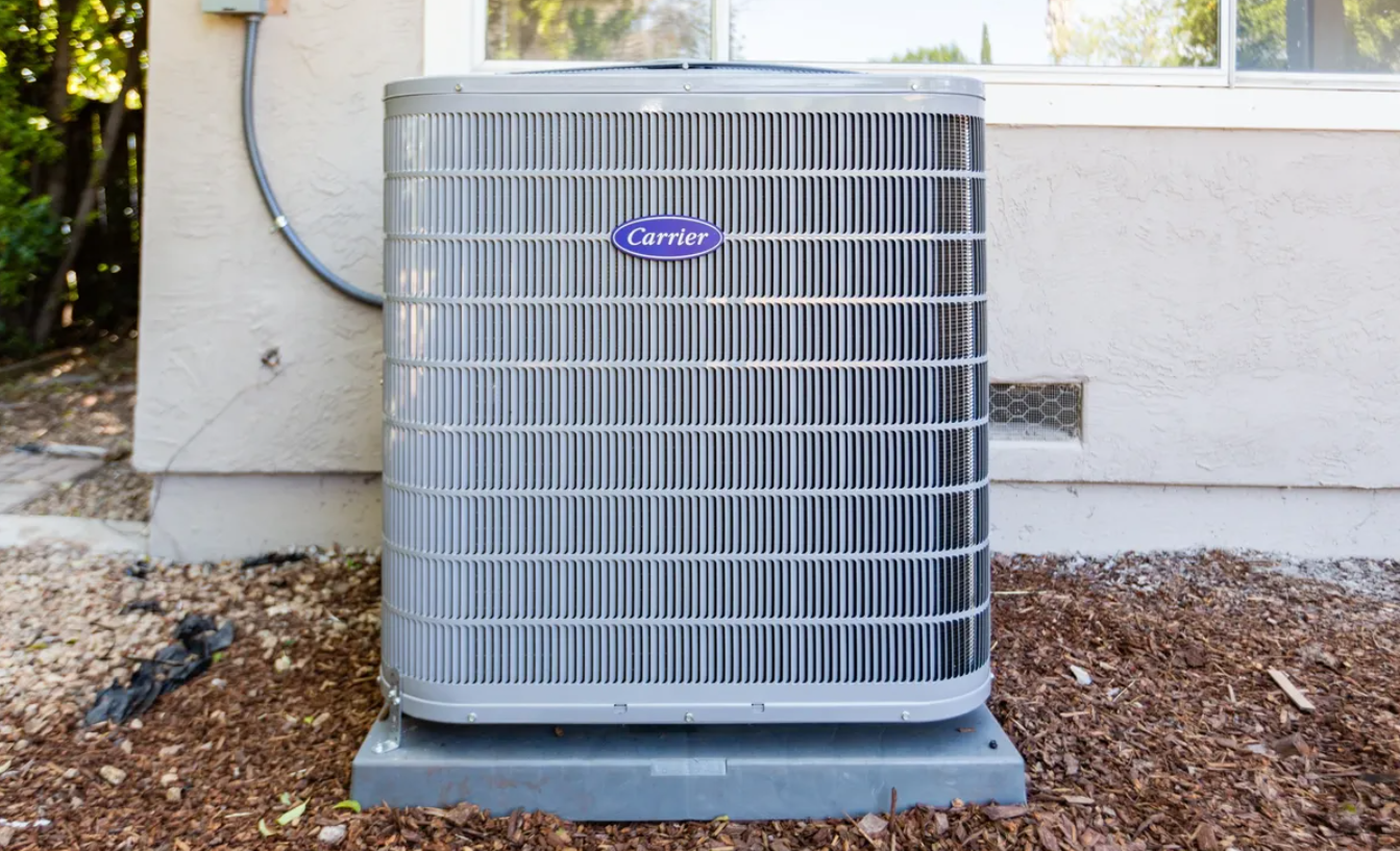 A carrier air conditioner is sitting outside of a house.