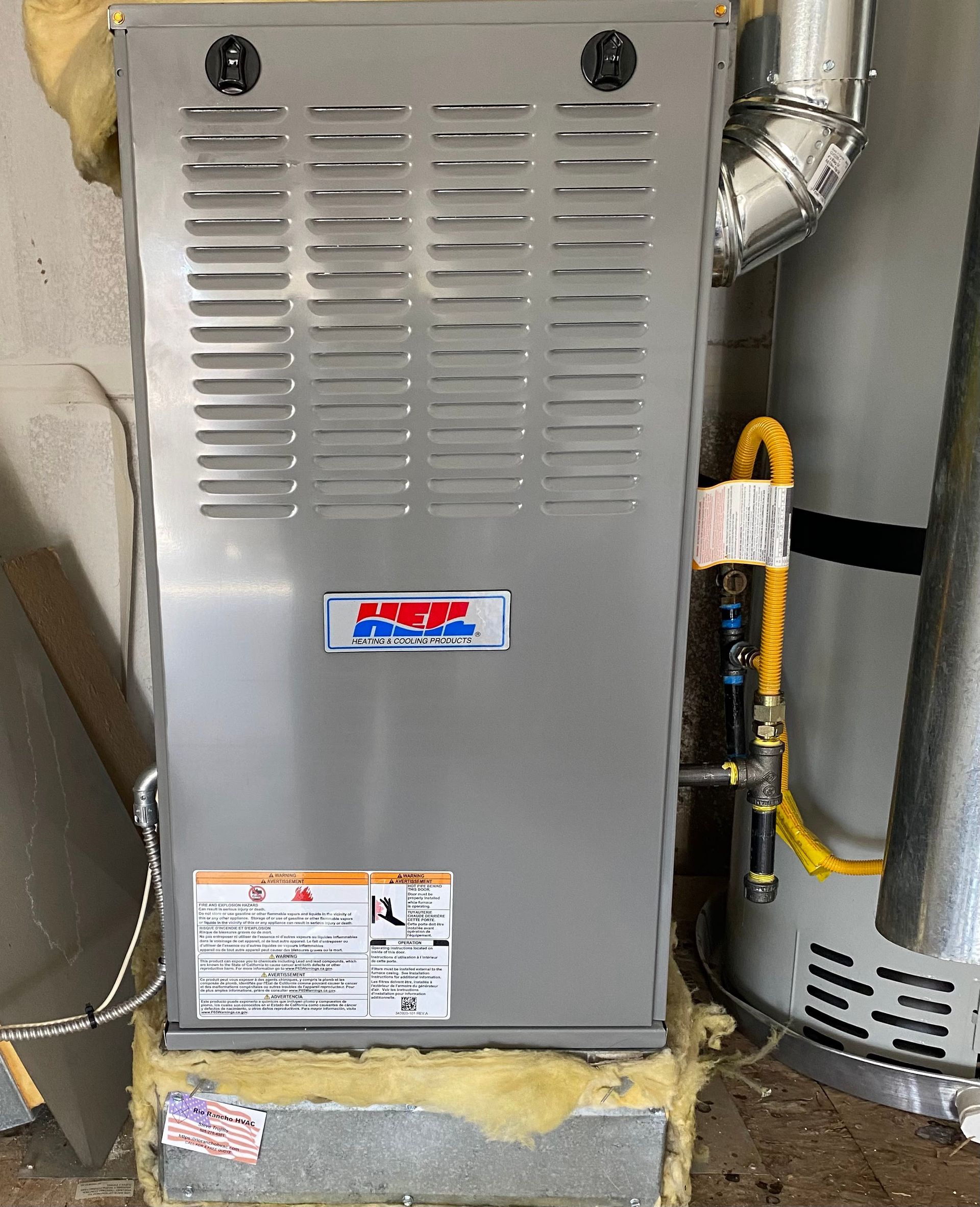 A stainless steel furnace is sitting next to a water heater in a garage.