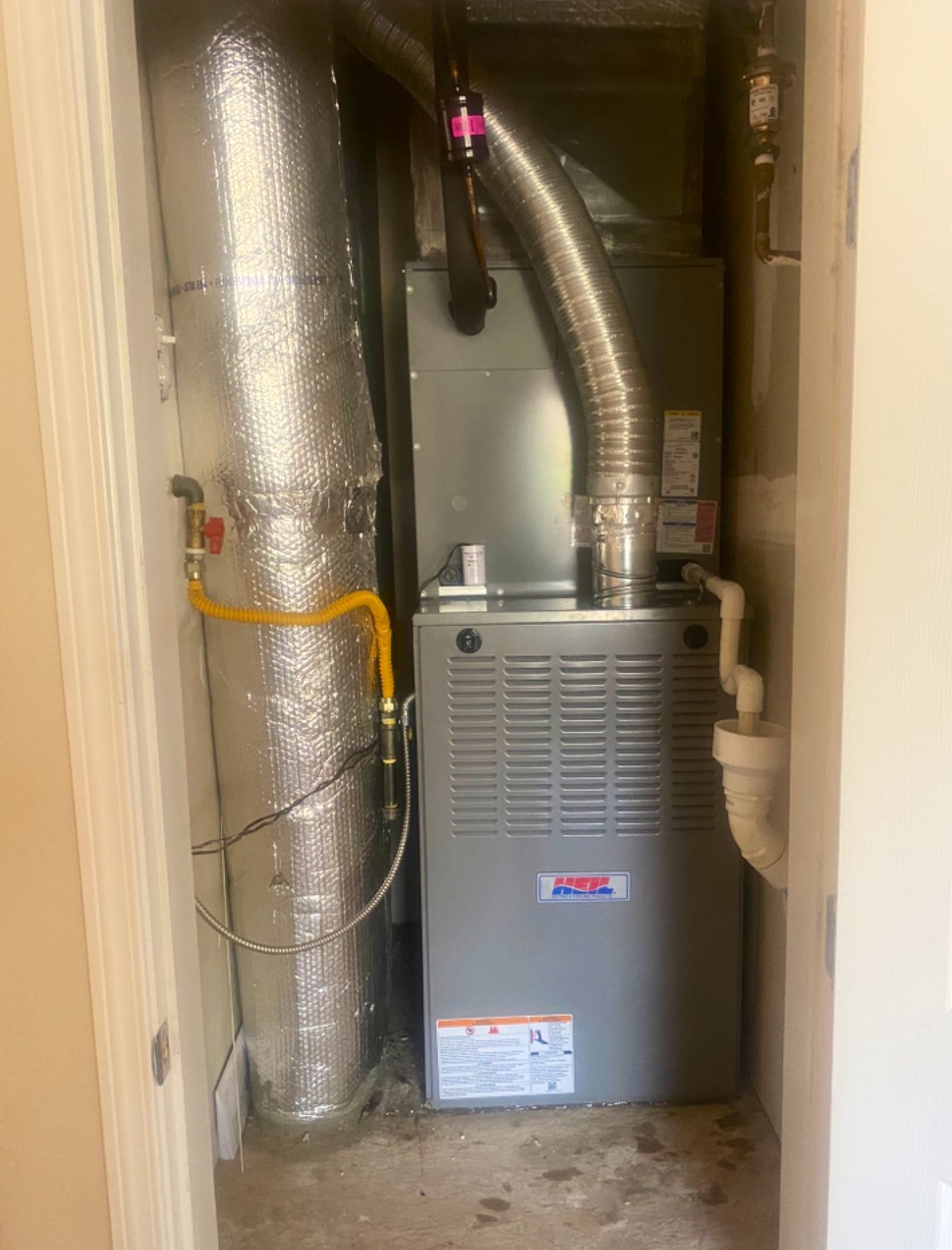 A furnace is sitting in a closet next to a pipe.