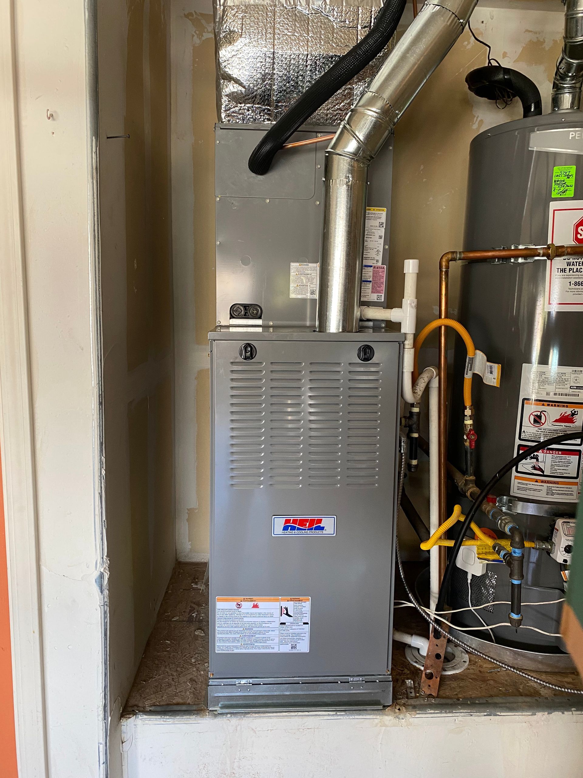 A furnace is sitting in a room next to a water heater.