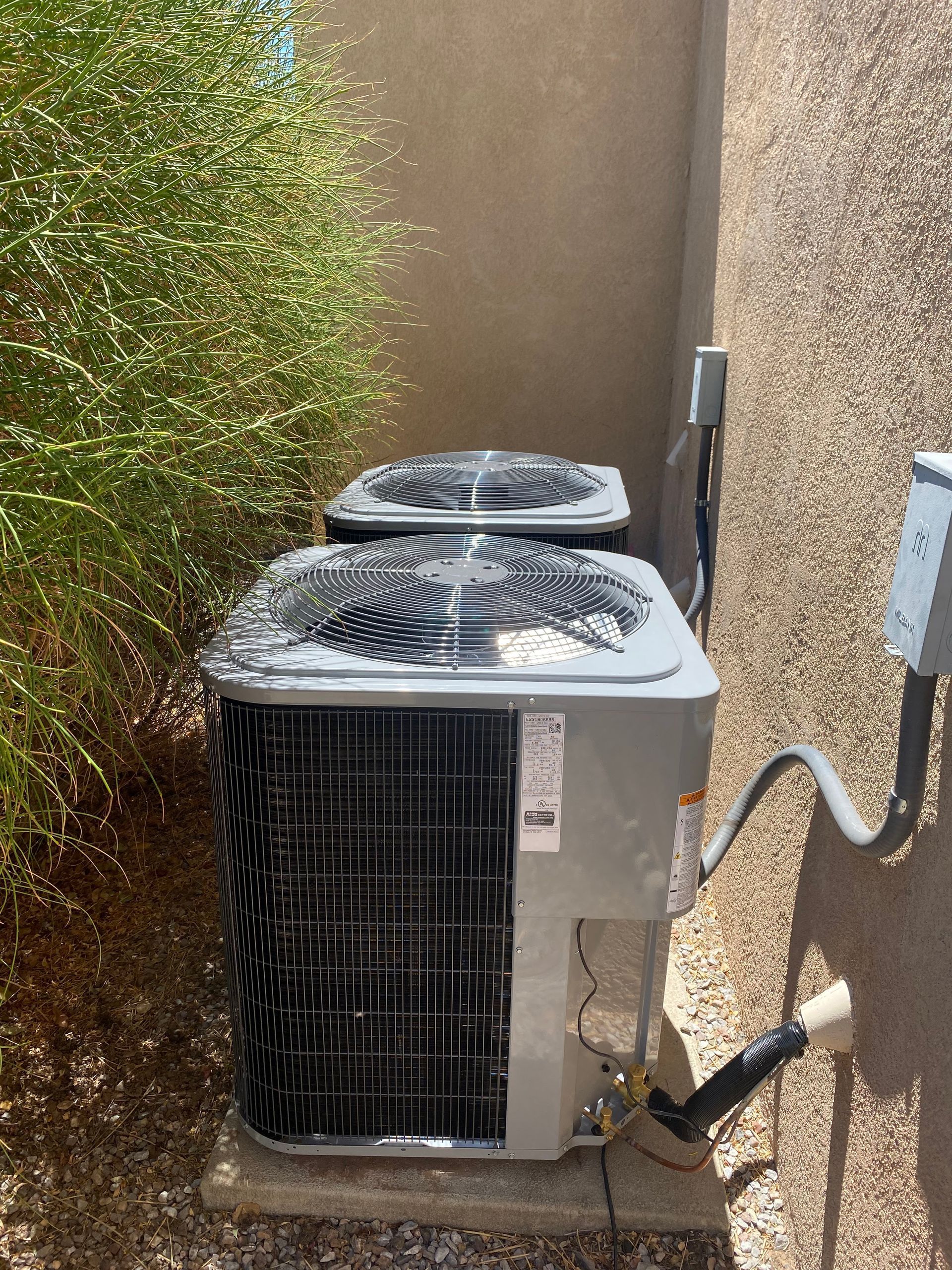 Two air conditioners are sitting next to each other on the side of a building.