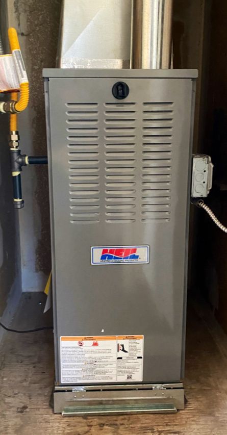 A gray furnace is sitting on a wooden floor in a room.