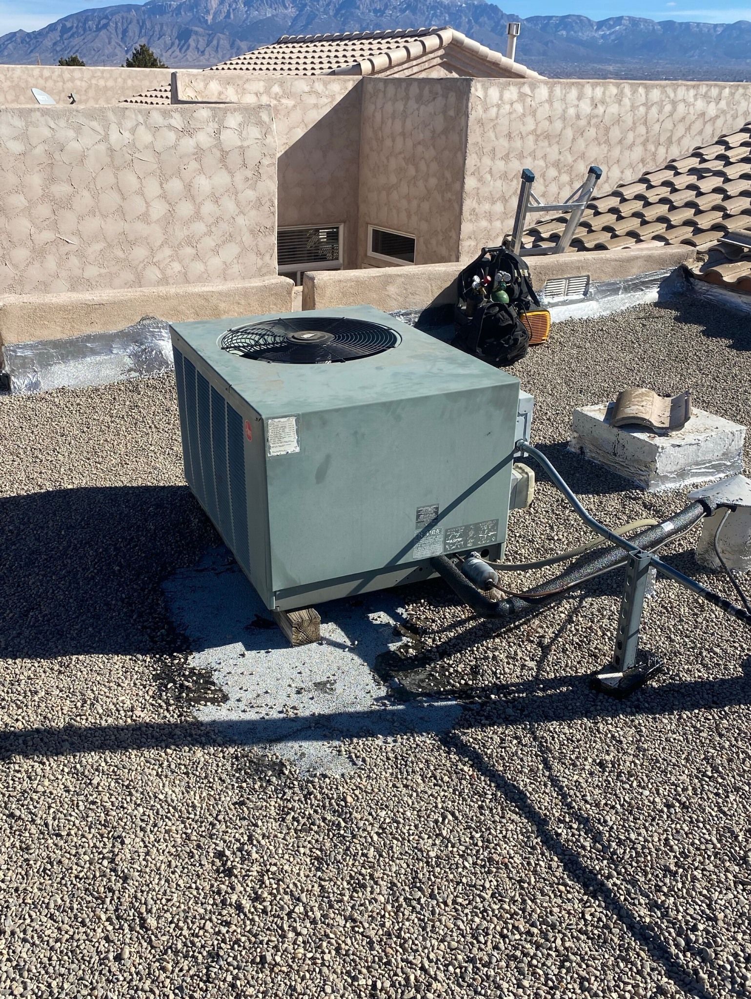 An air conditioner is sitting on top of a gravel roof.
