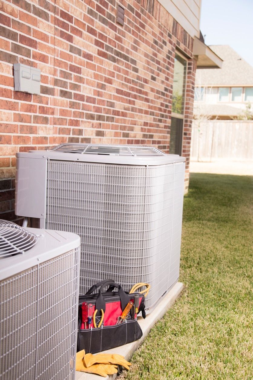 Two air conditioners are sitting next to each other on the side of a brick building.