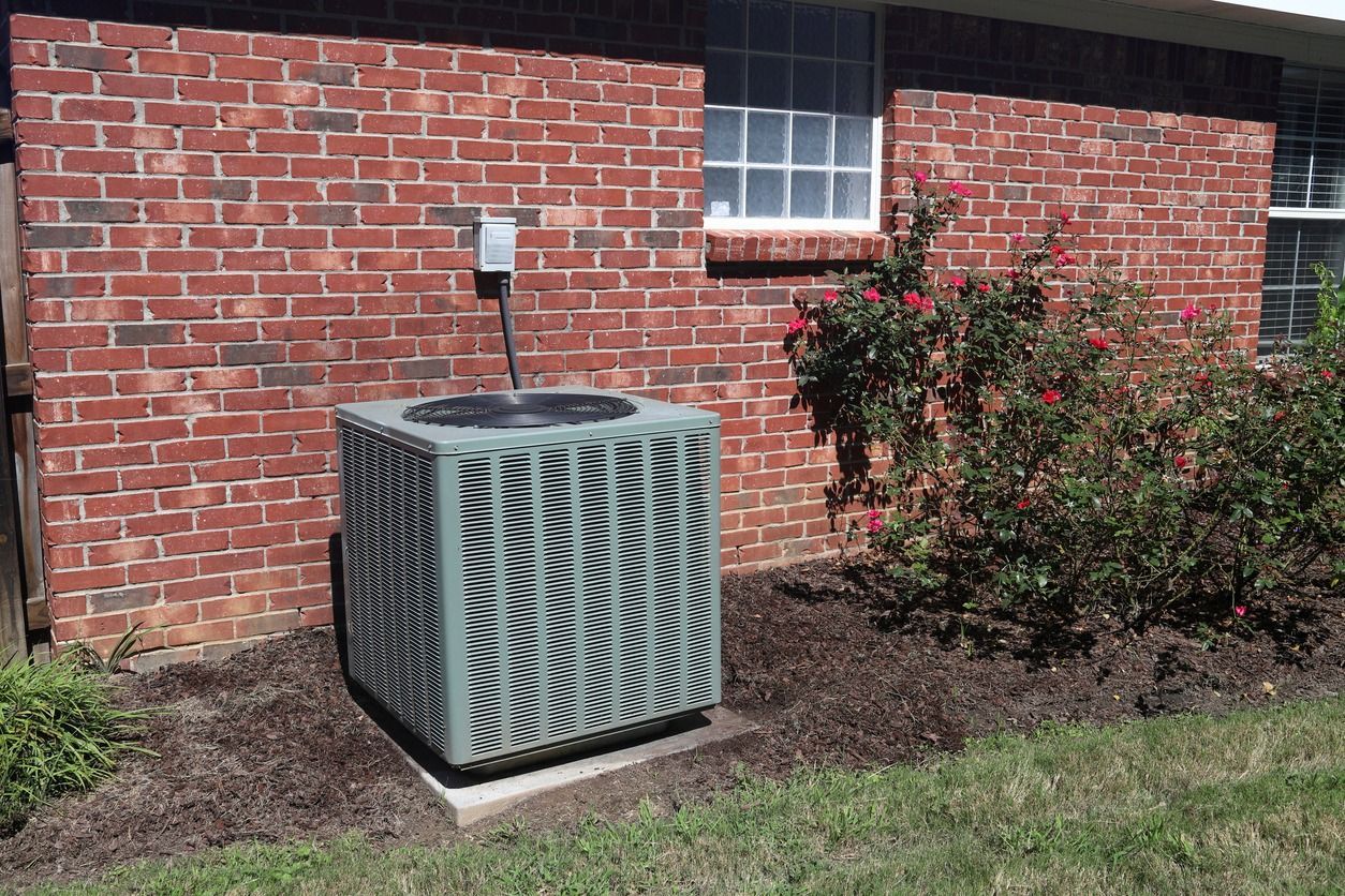 An air conditioner is sitting on the side of a brick house.