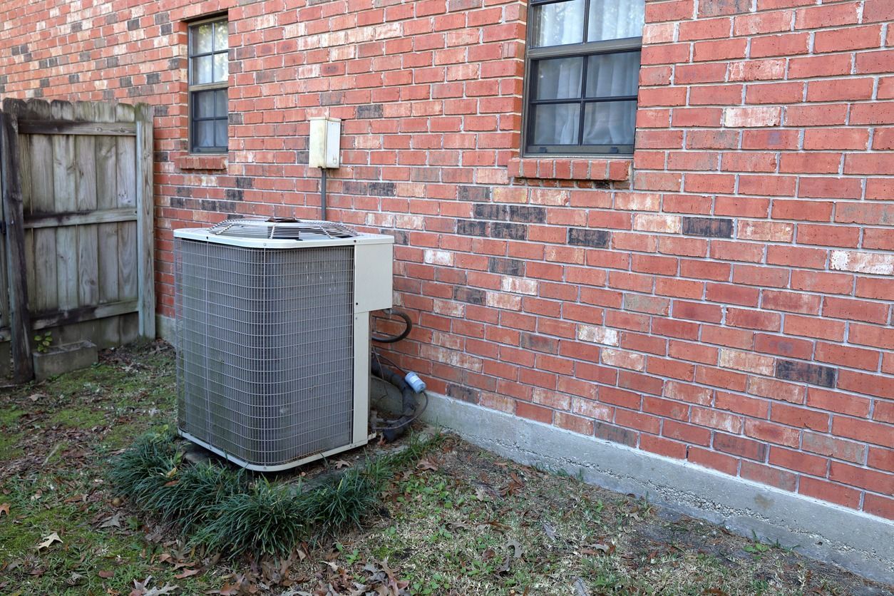 An air conditioner is sitting on the side of a brick building.