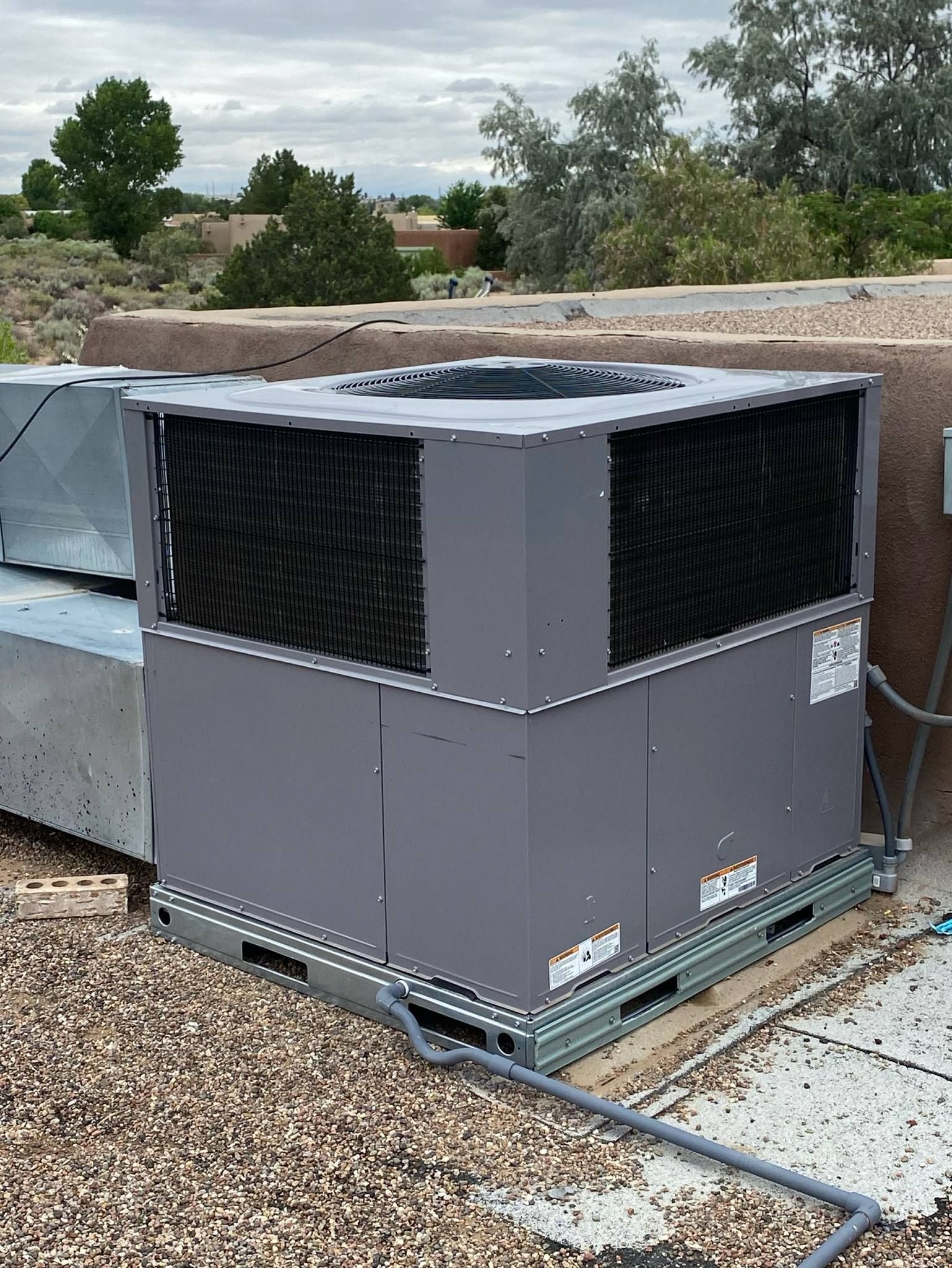 A large air conditioner is sitting on top of a gravel covered roof.