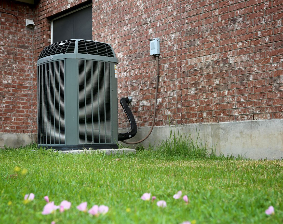An air conditioner is sitting on the side of a brick building.