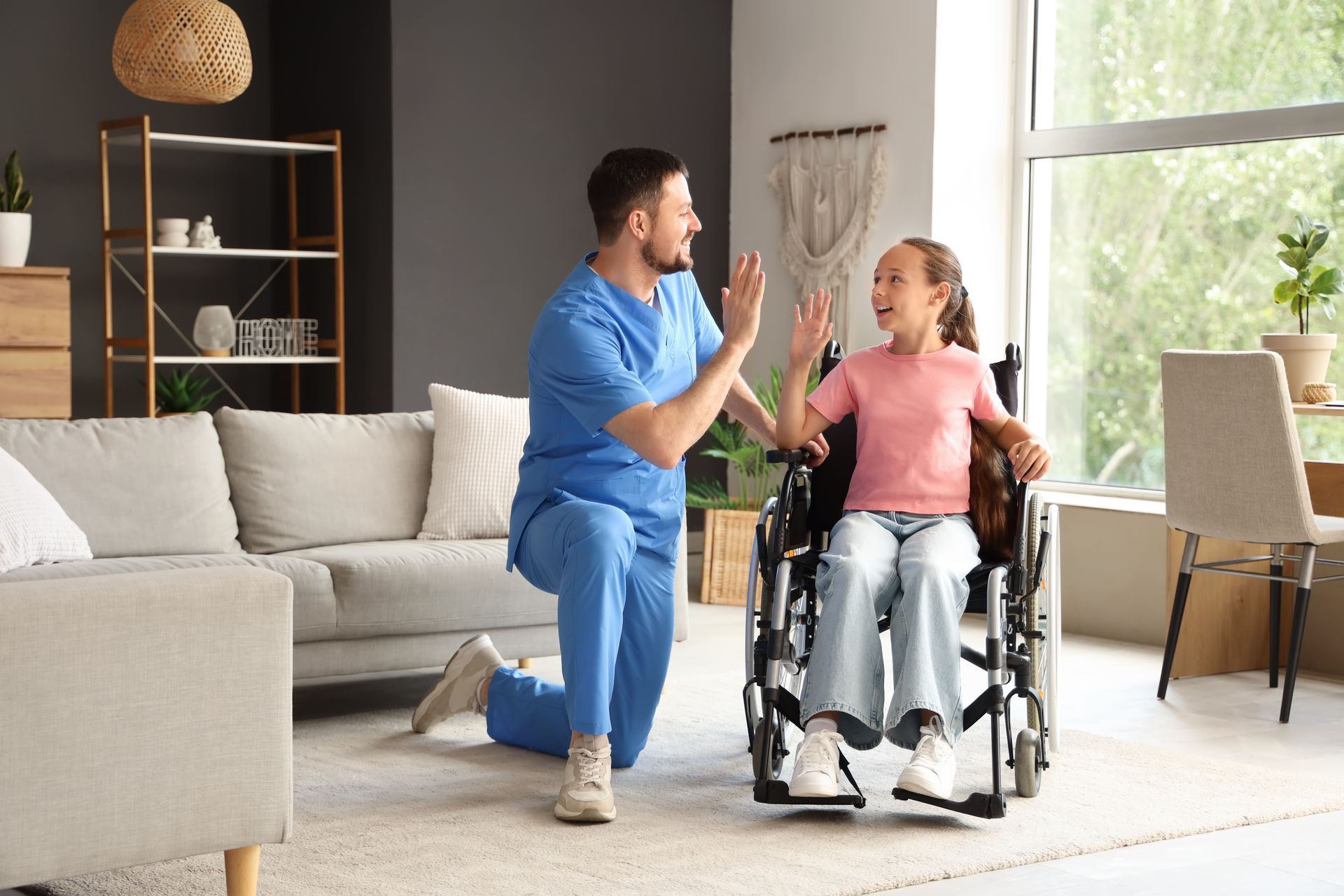 A young male doctor gives a high-five to a smiling young girl in a wheelchair.
