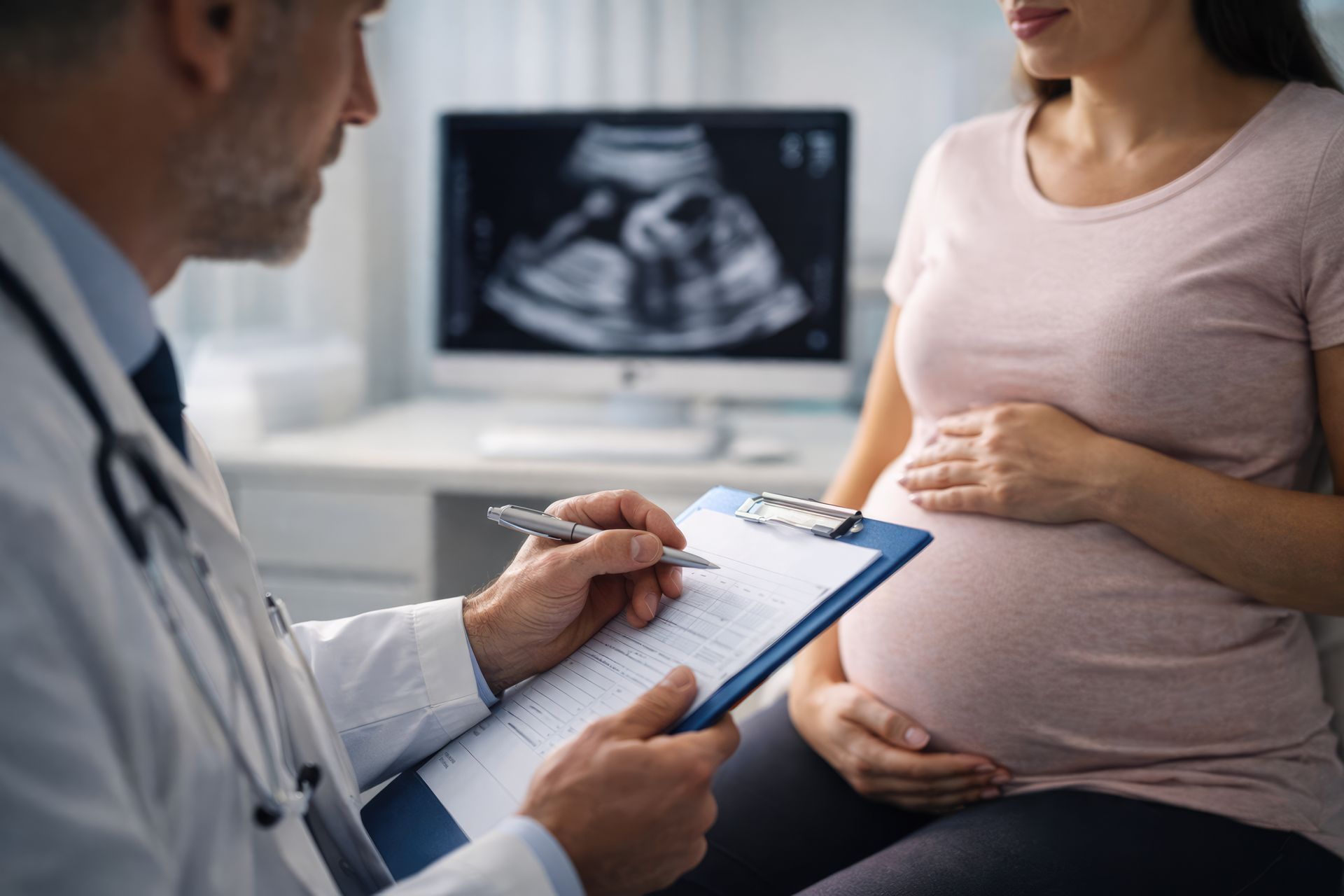 Prenatal checkup with doctor reviewing notes, patient seated, and ultrasound visible.