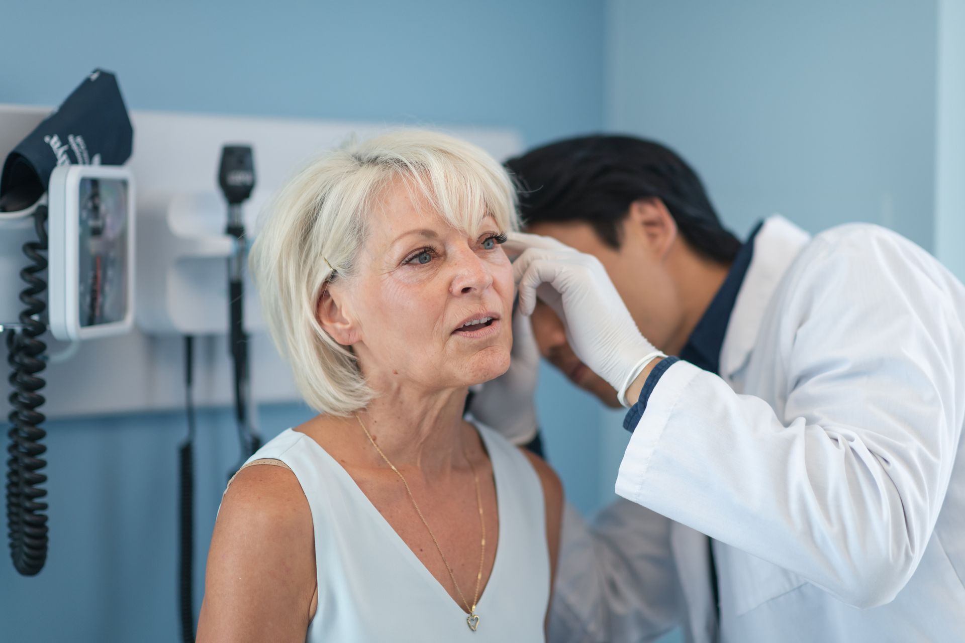 Male primary healthcare provider checks ear of older caucasian woman in a doctor’s office.