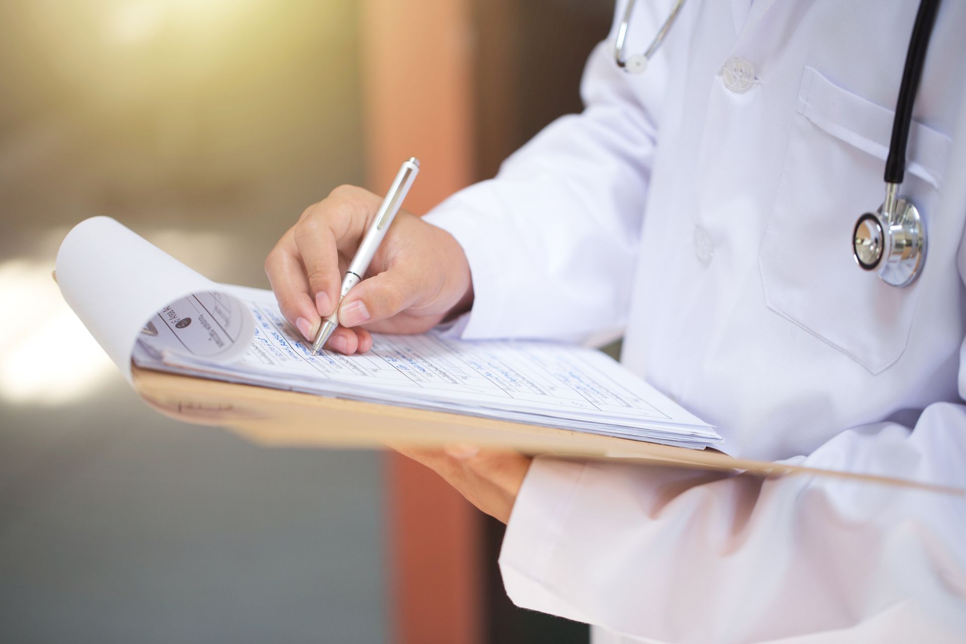 Close-up of doctor with stethoscope writing notes, highlighting primary care services.