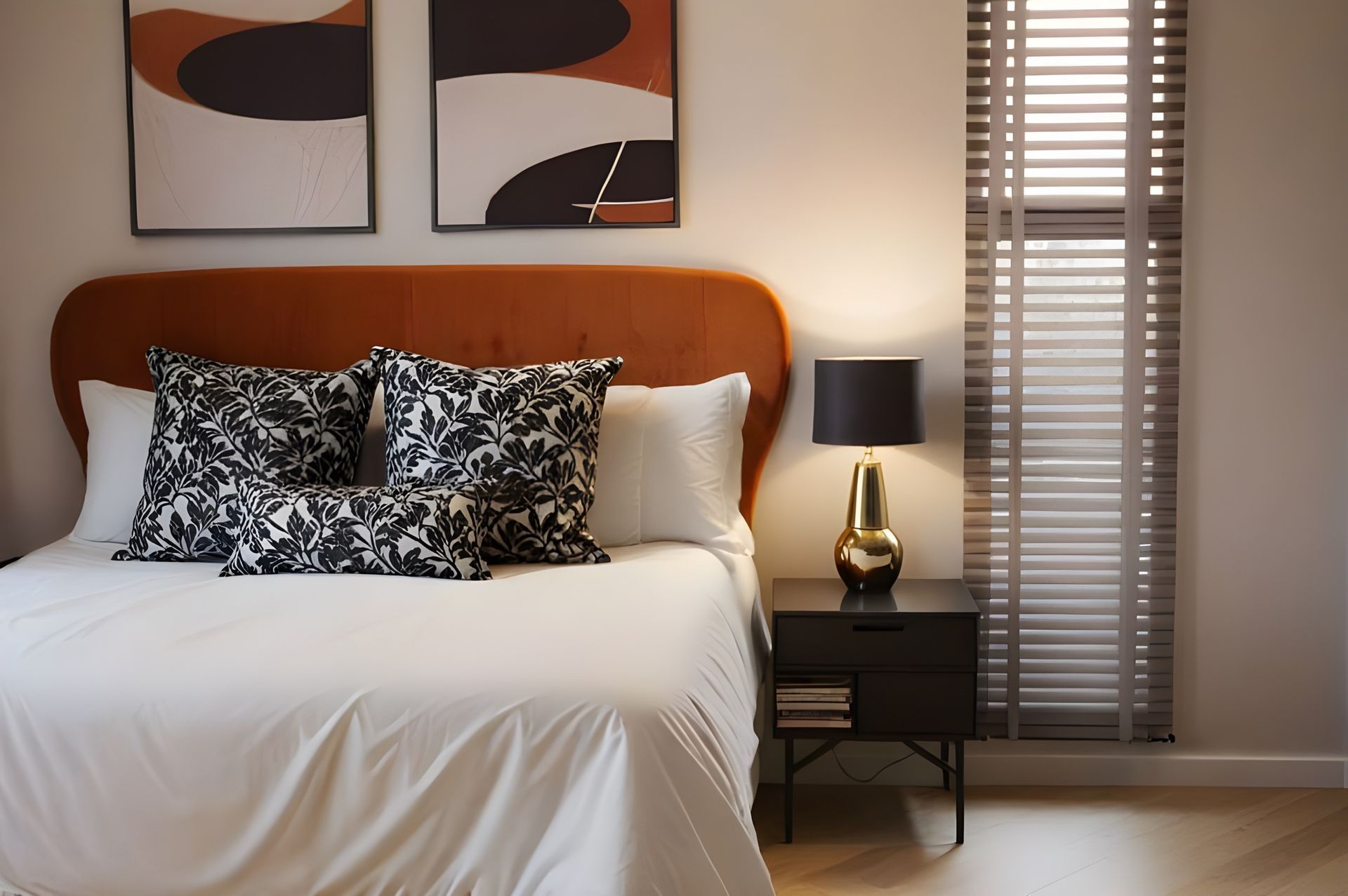 Bedroom with orange headboard, art, black and white pillows, and a gold lamp on a black nightstand.