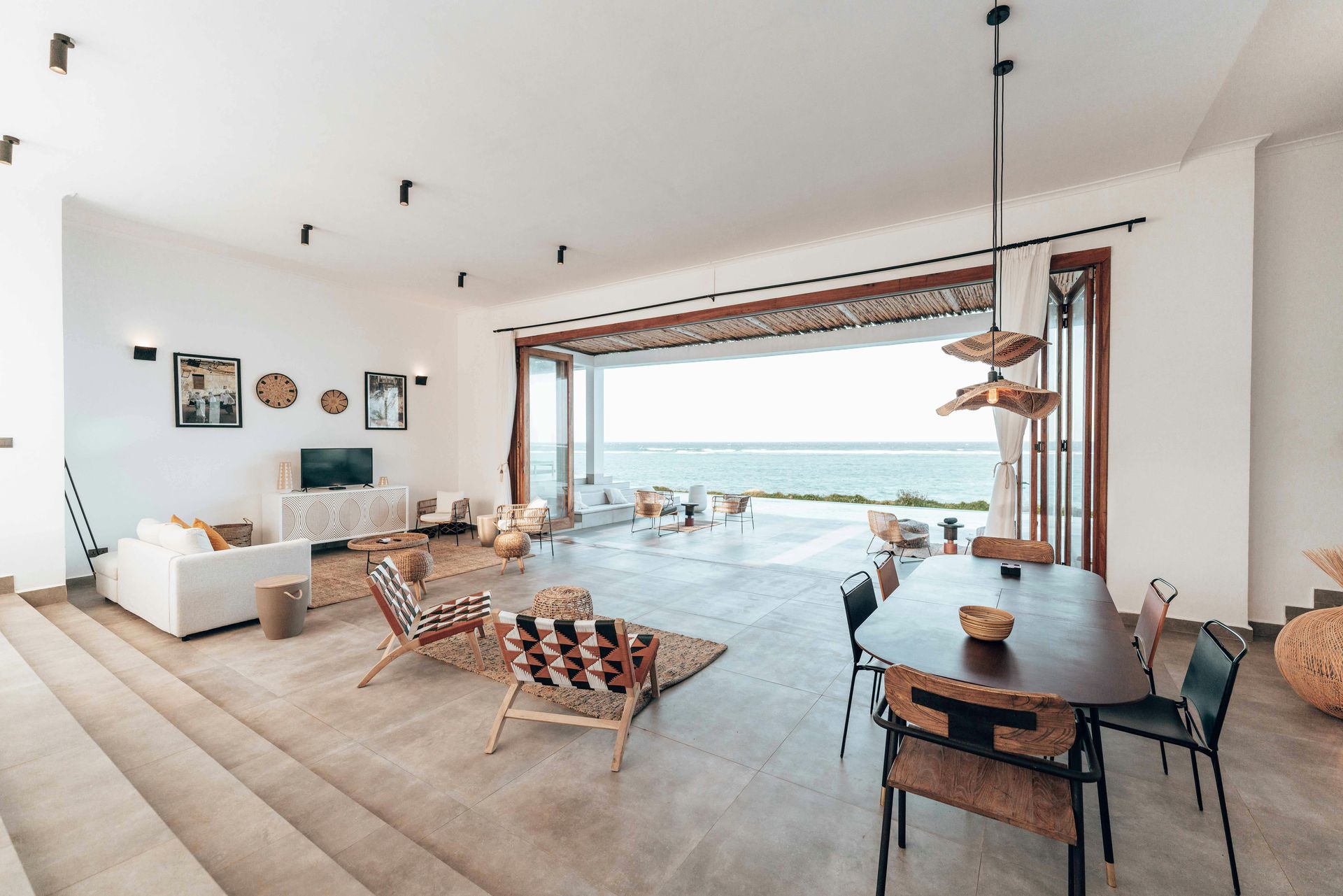 Spacious white-walled living area with ocean view, open doors, and modern furniture.
