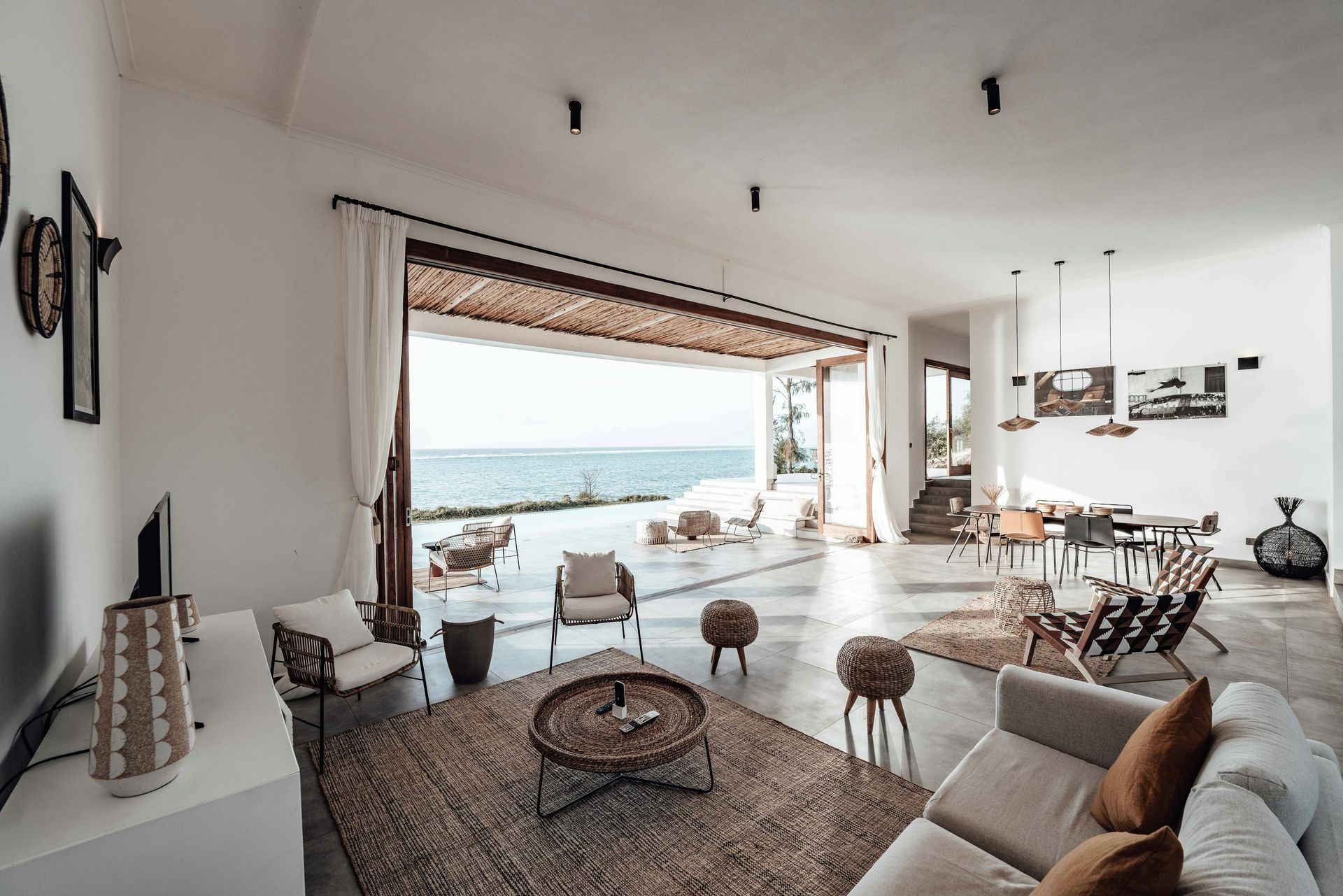 Spacious living room with ocean view; white walls, open doors, rattan furniture, neutral tones.