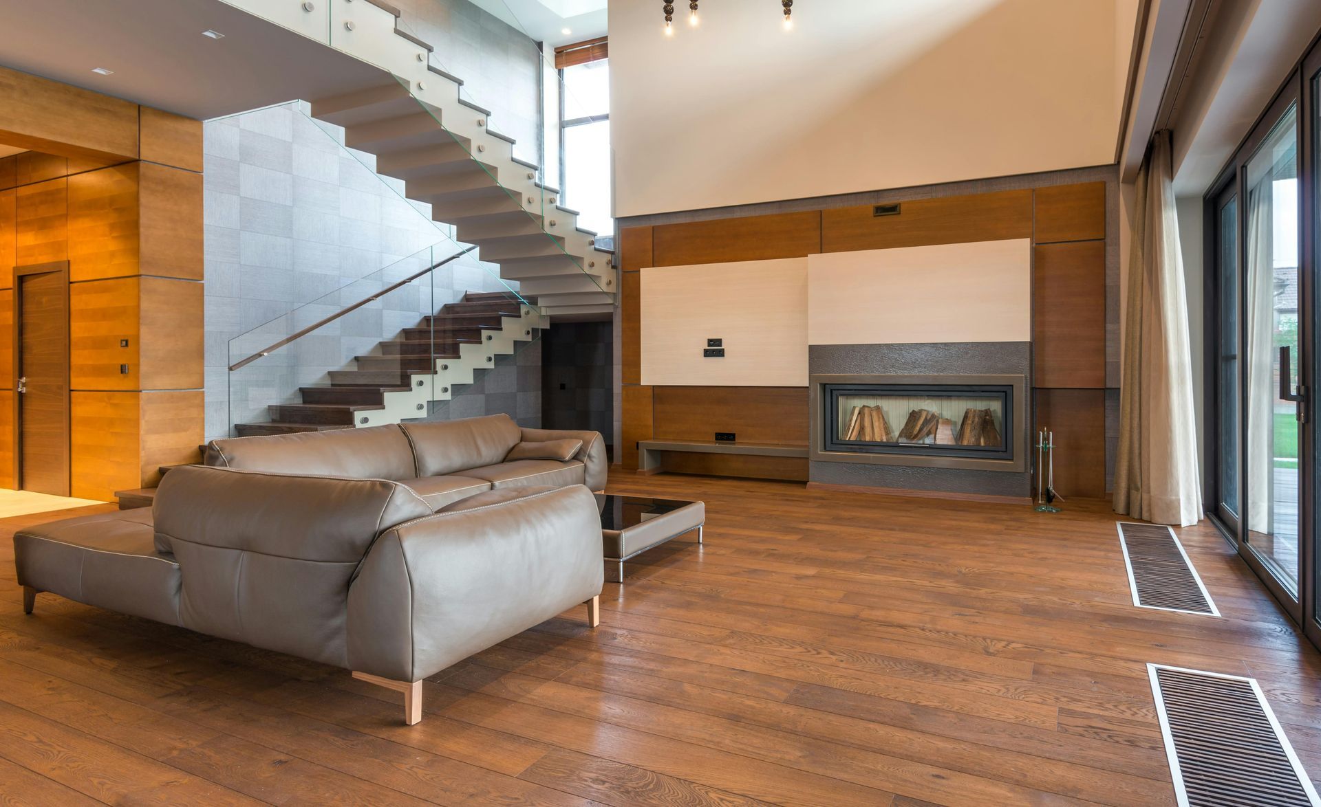 Modern living room with leather couch, fireplace, wooden floors, and staircase.