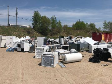 A pile of old appliances is sitting on top of a dirt field.