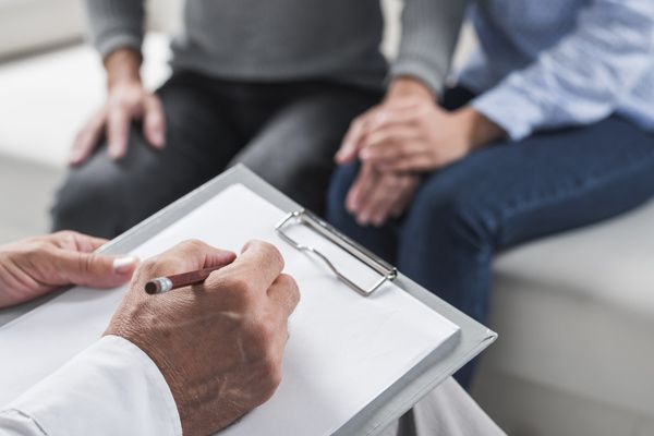 A doctor is writing on a clipboard in front of a couple.