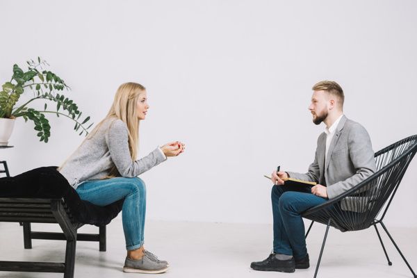 A man and a woman are sitting in chairs talking to each other.