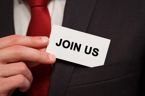 A man in a suit and tie is holding a card that says join us