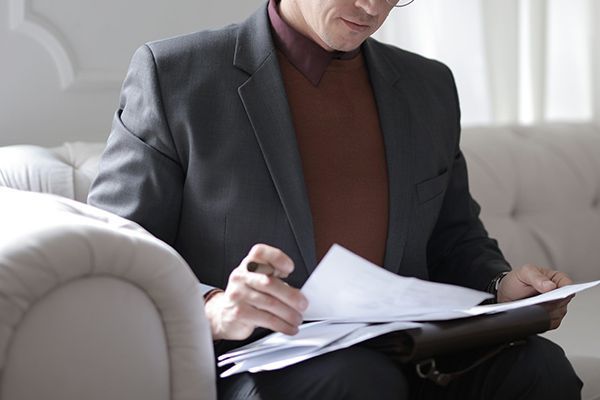 A man in a suit is sitting on a couch looking at papers.