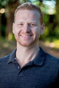 A man with a beard and a blue shirt is smiling for the camera.