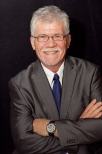 A man in a suit and tie is smiling with his arms crossed.