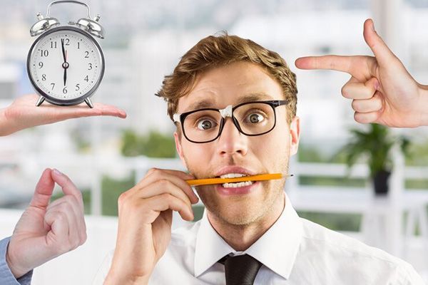 A man with a pencil in his mouth and a clock in the background.