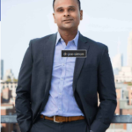 A man in a suit and blue shirt is standing with his hands in his pockets.