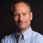 A man with a beard is wearing a blue shirt and tie.