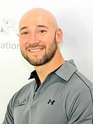 A bald man with a beard is wearing a gray under armour polo shirt.