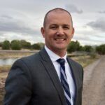 A man in a suit and tie is standing on a dirt road.