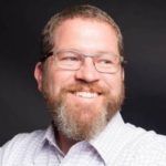 A man with a beard and glasses is smiling for the camera.