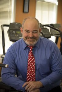 A man in a blue shirt and red tie is sitting in front of a treadmill.