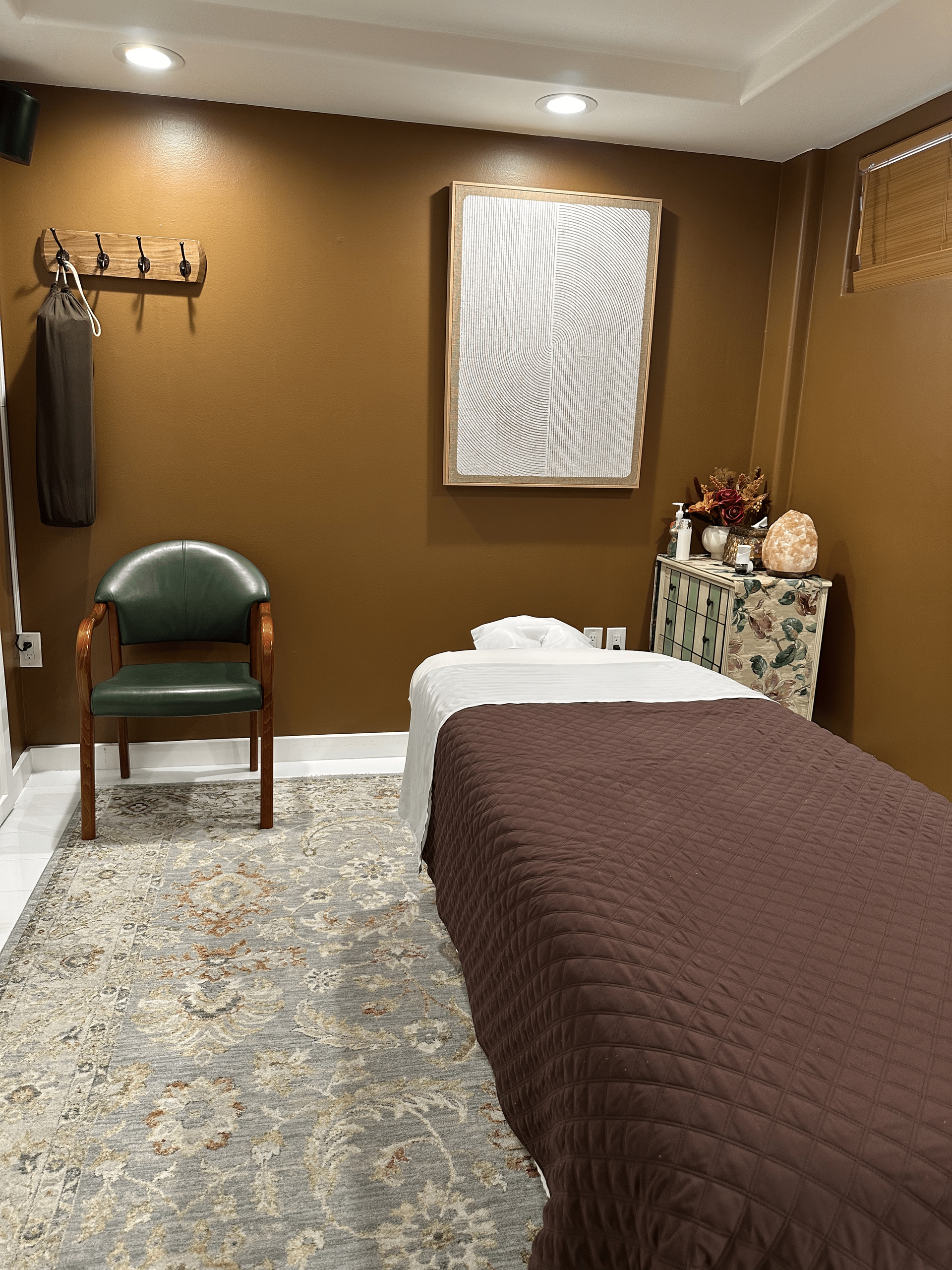 A massage room with two beds , a chair and a painting on the wall.