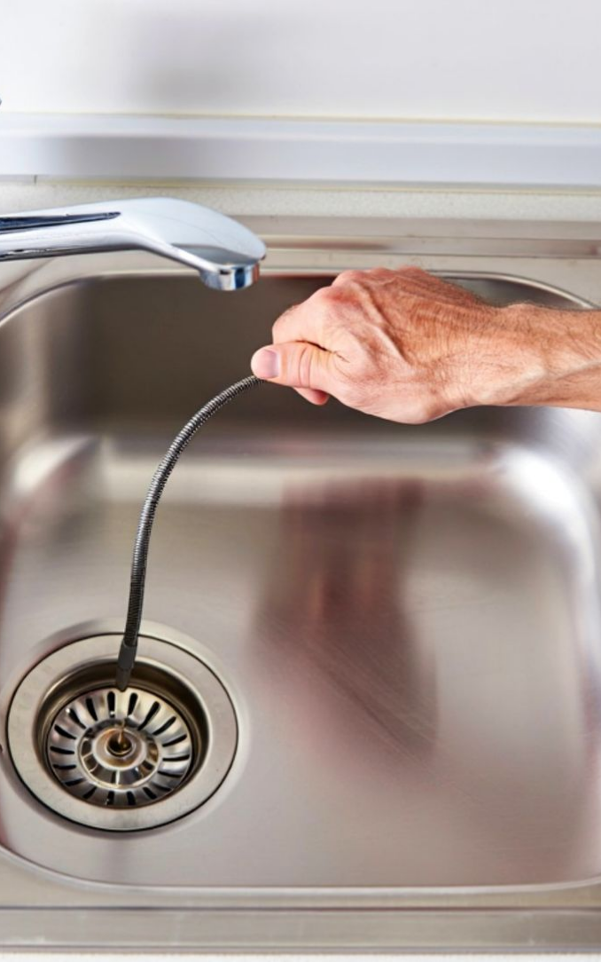 An experienced plumber clearing a clogged kitchen sink drain with specialized equipment. An experienced plumber clearing a clogged kitchen sink drain with specialized equipment.