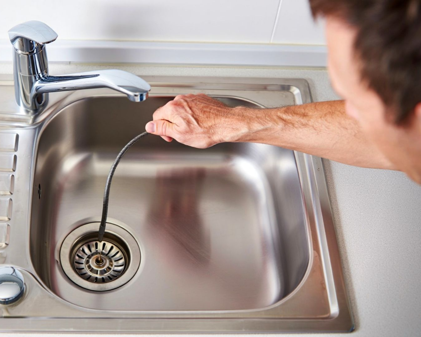 An experienced plumber clearing a clogged kitchen sink drain with specialized equipment. An experienced plumber clearing a clogged kitchen sink drain with specialized equipment.