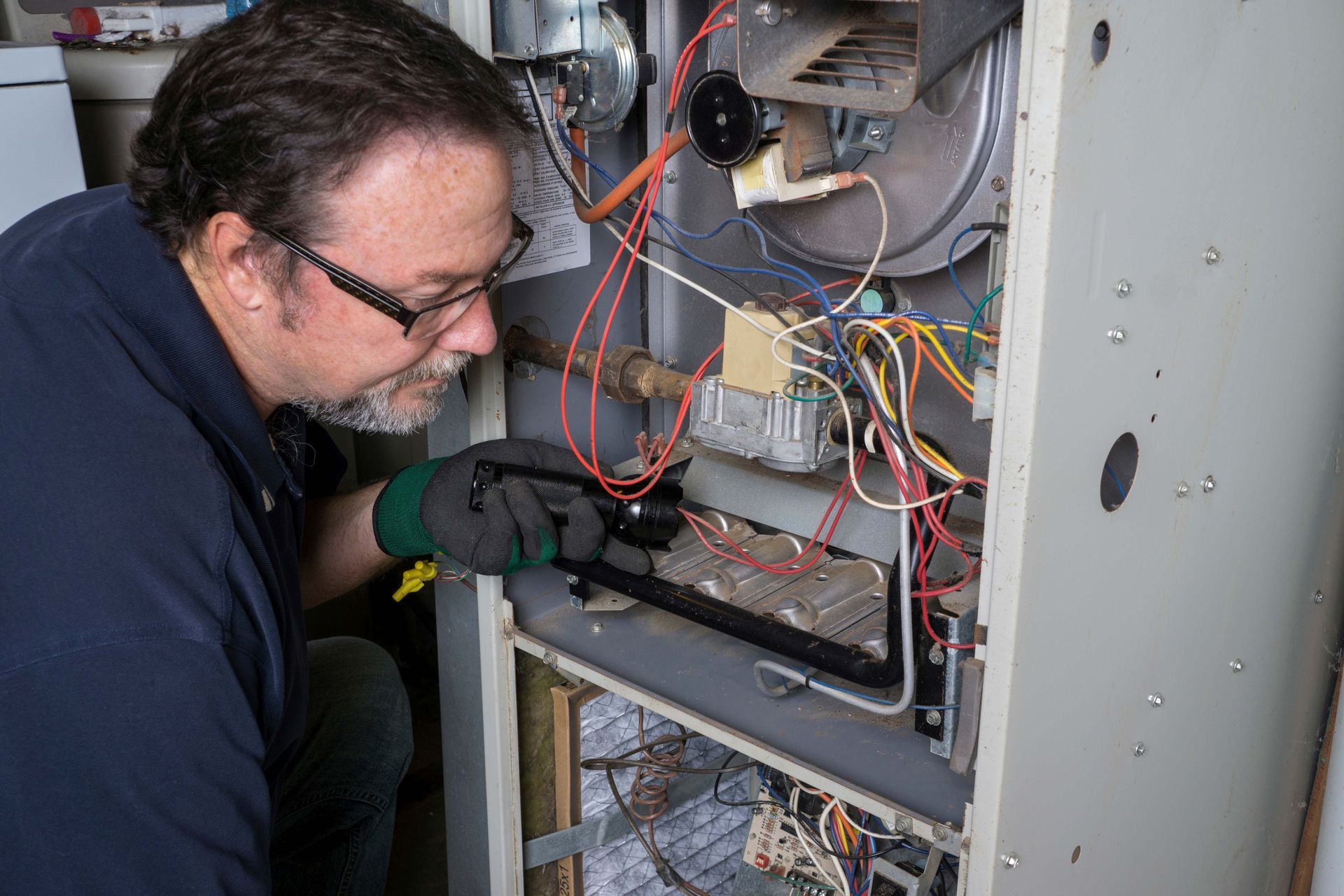 A technician looking over a gas furnace with a flashlight